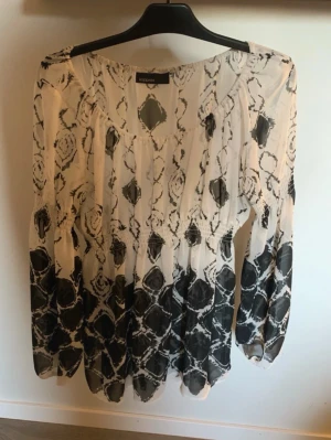 Vit och svart mönstrad blus - Snygg blus i vitt och svart från Redone med abstrakt mönster. Blusen har lång ärm, rundad halsringning och är tillverkad i ett tunt, lätt material som ger ett luftigt intryck. Perfekt för dig som gillar en avslappnad men trendig stil.