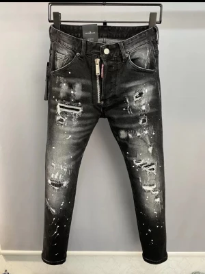 Dsquared2 jeans - Säljer ett par svarta jeans med slitningar och vita färgstänk för en edgy look. Jeansen har smal passform och flera hål och revor på både fram- och baksida. Perfekta för dig som gillar streetstyle och vill sticka ut.