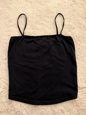 Svart crop top - Säljer en svart crop top från H&M Basic med tunna axelband och rak passform. Perfekt att styla till jeans eller kjol. Tillverkad i mjukt och stretchigt material för en bekväm känsla.