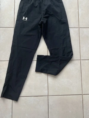Svarta träningsbyxor Under Armour - Säljer ett par svarta träningsbyxor från Under Armour med logga på vänster lår. Byxorna har resår i midjan och är tillverkade i ett lätt, funktionsmaterial som passar perfekt till träning och sportaktiviteter. Skicka gärna vid frågor och skicka gärna bud!