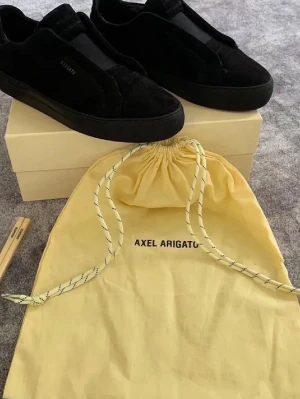 Svarta sneakers från Axel Arigato - Stilrena svarta sneakers från Axel Arigato i mocka med ton-i-ton sula och diskret logga på sidan. Klassisk låg modell med minimalistisk design och rundad tå. Levereras med originalpåse. Kan mötas upp