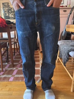 Carhartt Jeans - Säljer ett par mörkblå Carhartt jeans med raka ben och klassisk femficksmodell. Jeansen har kontrastsömmar och en lätt tvättad look för en avslappnad stil. Passar perfekt till en streetwear-outfit eller till vardags.