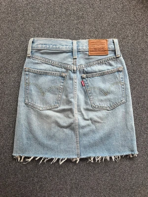 Levi's ljusblå jeanskjol med slitningar - Jättesnygg jeanskjol från Levi’s, ljus tvätt med slitningar. Strl W23. Highwaist passform.