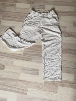 Beiga linnebyxor  - Snygga beiga linnebyxor med raka ben och klassisk passform. Byxorna har resår i midjan bak, knapp och dragkedja framtill samt sidfickor. Perfekta för en avslappnad och trendig stil. Materialet är luftigt linne som ger en skön känsla.