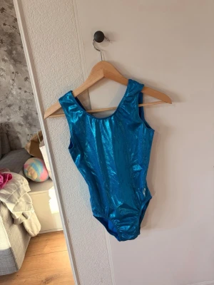 Blå glittrig gymnastikdräkt - Säljer en blå gymnastikdräkt med metallicglans och breda axelband. Dräkten är ärmlös och har rundad halsringning både fram och bak. Materialet är stretchigt och följsamt. Inte säker på storlek men tror runt 156 i barnstorlek. Köpte den ny för 400kr.