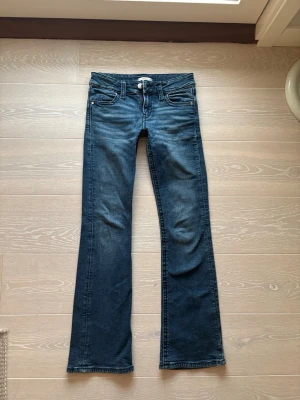 Mörkblå bootcut jeans från Gina Tricot - mörkblå bootcut jeans från Gina Tricot med klassisk femficksmodell och slitningar framtill. En knapp saknas andvänd 10-15 gånger en knapp där bak är tyvärr borta men hoppas det funkar🥰