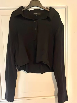 Svart croppad skjorta  - Svart croppad skjorta från XOXO Friends med klassisk krage och knäppning framtill. Skjortan har långa ärmar och en loose passform, perfekt för en avslappnad och trendig look.
