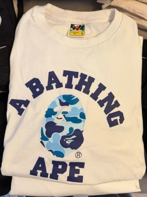 Vit A Bathing Ape t-shirt - Säljer en vit t-shirt från A Bathing Ape med stort tryck. Klassisk passform då denna sitter som en vanlig T-shirt. Köpt i Japan på Bapes officiella affär. Inget kvitto finns kvar. Sista bilder kompletteras för kontext. Endast använd 1-2 gånger.
