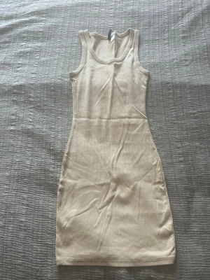 Beige ribbad ärmlös klänning - Säljer en beige, ribbad kortklänning med ärmlös design. Klänningen har en enkel och stilren form som passar perfekt till sommaren. Materialet är mjukt och stretchigt, vilket gör den bekväm att bära hela dagen.