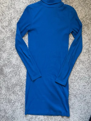 Blå långärmad poloklänning - Säljer en enkel och stilren blå klänning med polokrage och långa ärmar. Klänningen har en rak passform och är tillverkad i ett mjukt, stretchigt material som sitter bekvämt på kroppen. Perfekt för dig som gillar minimalistisk stil.