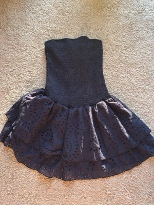 Mörkblå klänning med broderade detaljer - Supersnygg mörkblå klänning med bred smock i midjan och dubbla volanglager. Klänningen har broderade hålmönster som ger en unik look och passar perfekt till en trendig outfit. Materialet känns mjukt och följsamt, och volangerna ger extra volym.