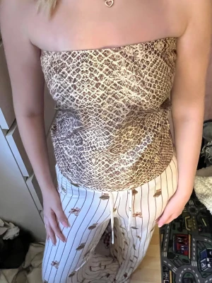 Beige tubtopp med ormmönster - Säljer en beige tubtopp med ormmönster. Toppen är axelbandslös och har en croppad passform som sitter snyggt på kroppen. Perfekt för dig som vill sticka ut med ett trendigt mönster och en cool vibe.