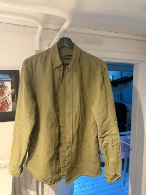 Olivgrön linneskjorta regular fit från Cubus - Säljer en olivgrön skjorta i 100% linne med regular fit. Skjortan har klassisk krage, knappar framtill och långa ärmar. Perfekt för dig som gillar en avslappnad men ändå stilren look.