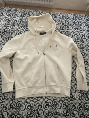 Vit hoodie med dragkedja från Polo Ralph Lauren - Säljer en Polo Ralph Lauren zip hoodie i benvit färg, storlek L (upplevs något liten i storleken). Köpt på Polo Ralph Lauren Outlet i Hede Fashion Outlet, Kungsbacka. Nypris 1 500 kr och kvitto finns kvar. Den är använd men är i väldigt fint skick. Pris går att diskuteras och fler bilder kan skickas, bara att höra av sig.