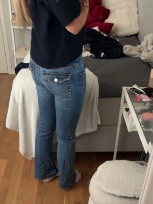 Blå bootcut jeans med fickdetalj - Säljer ett par klassiska blå bootcut jeans med snygg fickdetalj bak och knapp. Jeansen har normalhög midja och är i ett mjukt denimtyg. Passar perfekt till en avslappnad och trendig stil.