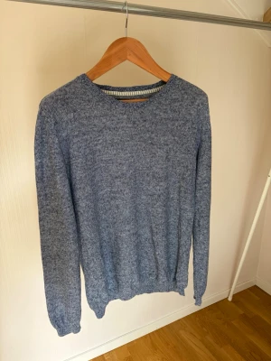 Blåmelerad stickad tröja - En enkel och stilren blåmelerad stickad tröja med rund halsringning och långa ärmar. Tröjan har ribbade muddar vid ärmslut och nederkant. Perfekt för lager på lager och passar till det mesta i garderoben.