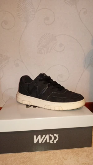 Svarta skor - Snygga svarta sneakers från Warp med vit sula och klassisk snörning. Skorna har en stilren design med diskreta detaljer och är tillverkade i syntetmaterial. Perfekta för dig som vill ha en clean och sportig look.