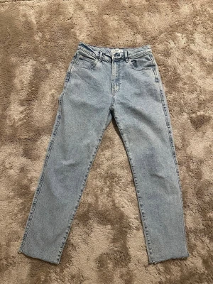 Ljusblå mom jeans från Pull&Bear - Ljusblå mom jeans från Pull&Bear med hög midja och raka ben. Klassisk femficksmodell med dragkedja och knapp framtill. Jeansen har en vintageinspirerad tvätt och är tillverkade i denim.