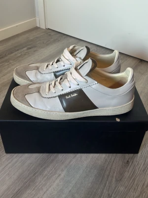 Paul Smith (sällsynta) - Snygga sällsynta sneakers från Paul Smith i vitt och ljusgrått läder med grå mockadetaljer och en mörkgrå panel på sidan. Klassisk låg modell med vita skosnören och diskret logga på sidan. Perfekta för en stilren och avslappnad look. Nypris: 4100 kr. Hör av er vid frågor, allt gott! 