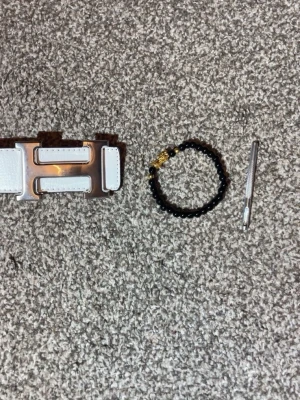 Vitt H skärp med silverdetaljer - Säljer ett stilrent vitt skärp från H med en stor, blank silverfärgad H-spänne. Skärpet är gjort i slätt skinn och har tydliga sömmar längs kanterna. Perfekt accessoar för att lyfta din outfit.