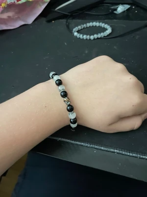 Två pärlarmband i svart och grått - Säljer två snygga armband med pärlor, ett med svarta och grå pärlor i mönster och ett med enbart grå pärlor. Båda är elastiska och passar de flesta handleder. Perfekta accessoarer för att lyfta din stil.