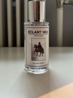 Éclant 149.0 extrait de parfum - En stilren parfymflaska i genomskinligt glas med silverfärgad spraykork. Etiketten har en bild på en ryttare och texten 'Éclant 149.0 extrait de parfum'. Parfymen har en modern och minimalistisk design som känns exklusiv. 140ml kvar