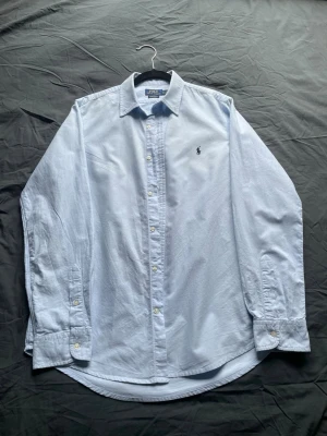 Ljusblå skjorta från Ralph Lauren - Klassisk ljusblå skjorta från Ralph Lauren. Skjortan har lång ärm, knappar framtill och klassisk krage. Perfekt för en stilren look och enkel att matcha med jeans eller chinos.