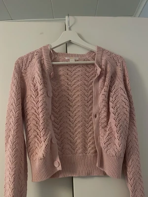 Rosa stickad kofta från gina - Söt rosa stickad kofta med genomgående knappar framtill och ribbade muddar. Koftan har ett hålmönster och är croppad i modellen.   Har bara använt den 1-3 gånger.