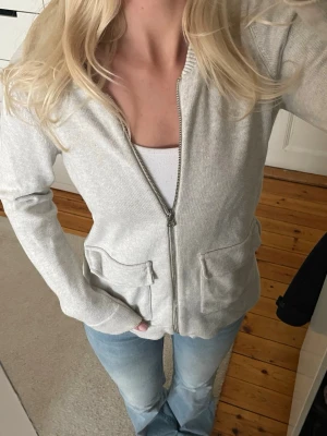 Grå kofta med dragkedja - Jättefin stickad kofta/tunn jacka med silver dragkedja. Ljusgrå färg och ribbad krage. Koftan har två fickor framtill.   Köpt second hand, jättebra skick.