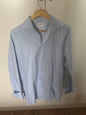 Skjorta från Lindbergh - Snygg blåvit randig skjorta från Lindbergh i slim fit-modell. Tillverkad av ekologisk bomull som känns mjuk och skön mot huden. Klassisk krage, knäppning framtill och långa ärmar. Perfekt för en clean och stilren look.