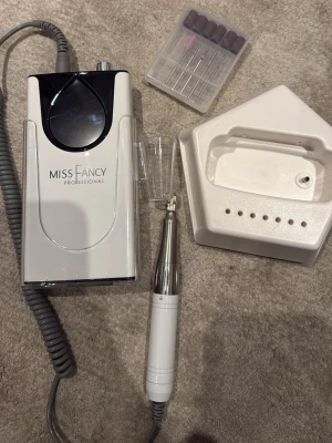 Nagelfilmaskin Miss Fancy Professional - Elektrisk nagelfilmaskin från Miss Fancy Professional i vit och silver. Inkluderar flera sliphuvuden och en praktisk hållare för maskinen. Perfekt för att fixa naglarna hemma med proffsigt resultat. Använt den väldigt sparsamt och biten är helt oanvända. Nypris är 2599kr 