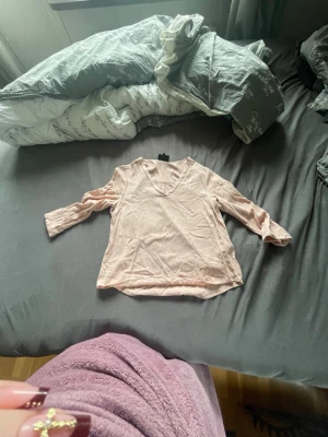 Ljusrosa blus med V-ringning - Söt ljusrosa blus med V-ringning och trekvartsärm. Blusen har en avslappnad passform och är tillverkad i ett tunt, mjukt tyg som ger en skön känsla. Perfekt att styla med jeans eller kjol för en trendig look.