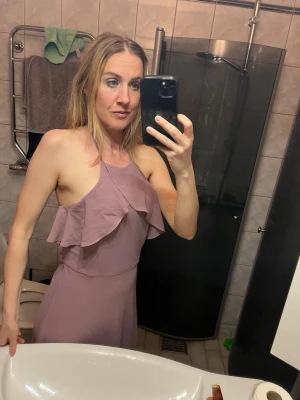 Ljuslila halterneckklänning med volang - Säljer en ljuslila långklänning med halterneck och volangdetalj framtill. Klänningen är ärmlös och har en elegant, feminin siluett. Perfekt för sommarens tillfällen och passar dig som gillar en stilren look med en twist. Använd endast en gång.