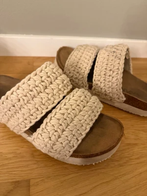 Beige stickade sandaler - Säljer ett par snygga sandaler från märket INVXE med två breda, stickade band i beige bomull. Sandalerna är i storlek 40 men passar även 39 som jag har.  Perfekta för en chill och trendig look i sommar. sandalerna är lite smutsiga mot sulan men går att tvätta bort enkelt .
