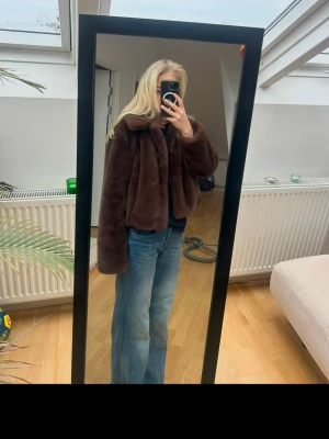 Brun pälsjacka med krage - Säljer en snygg brun pälsjacka(inte riktigt päls) med bred krage och avslappnad passform. Jackan är kortare i modellen och har långa ärmar. Perfekt för att hålla sig varm och stilren under kalla dagar. Materialet är mjukt och fluffigt för en lyxig känsla. Har vanligt storlek s