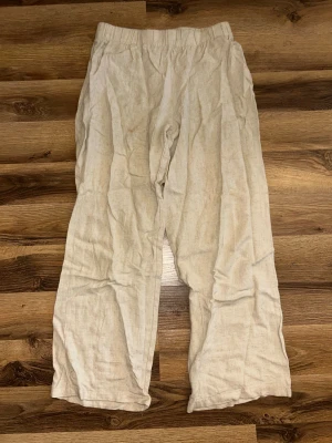 Beiga vida linnebyxor - Snygga och avslappnade linnebyxor i beige med bred passform och resår i midjan. Perfekta för en chill och stilren look. Tillverkade i mjukt linnematerial som andas bra.