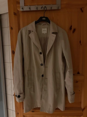 Beige trenchcoat från Jack and Jones  - Stilren beige trenchcoat från jackandjones med klassisk krage, knäppning framtill och två fickor. Lätt oversized passform och snygga detaljer vid ärmslut. Perfekt för lager-på-lager och enkel att matcha med olika outfits.