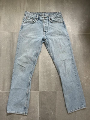 Ljusblå raka jeans från Zara - Klassiska ljusblå jeans från Zara med rak passform och fem fickor. Jeansen har normal midja, bälteshällor och stängs med knapp och dragkedja. Perfekta för en avslappnad och tidlös stil. Lite sliten vid ena fram fickan, se bild 2