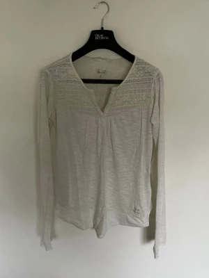 Vit långärmad blus med spetsdetaljer från odd Molly  - Söt vit långärmad blus från Cream med v-ringning och spetsdetaljer upptill. Blusen har en avslappnad passform och dekorativa knappar i nacken. Perfekt för dig som gillar romantiska och feminina detaljer.