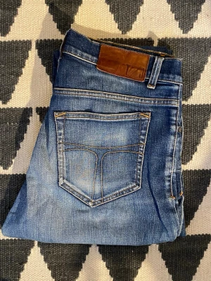 Blå jeans från tiger of sweden  - Snygga blå jeans från tos med klassisk femficksdesign och bruna kontrastsömmar. Jeansen har en skinnpatch bak i midjan och subtila slitningar för en cool look. Tillverkade i denim med lätt stretch för extra komfort.
