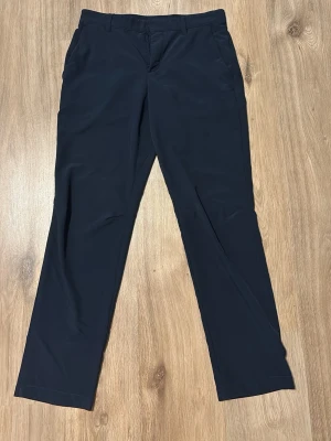 Mörkblå golfbyxor med rak passform storlek 30/32  - Mörkblå golfbyxor med klassisk rak passform och enkel design. Byxorna har hällor för skärp, dragkedja och knapp framtill. Materialet är lätt och smidigt, perfekt för träning eller aktiva dagar.