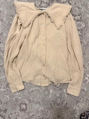 Beige blus med stor krage från Boii - Supersöt beige blus från Boii med stor volangkrage och knappar framtill. Långärmad modell med lätt rynkade ärmar och breda muddar. Perfekt för dig som gillar romantisk och trendig stil. 100% bomull. Köpt på Sellpy men aldrig använd av mig.💝