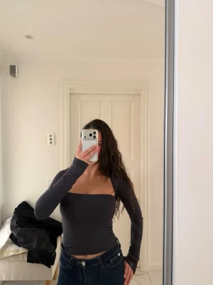 Mörkgrå långärmad topp med fyrkantig ringning - Trendig mörkgrå topp med lång ärm och fyrkantig ringning. Sitter tight och har en croppad passform som framhäver midjan. Perfekt att styla med jeans eller kjol för en cool look.