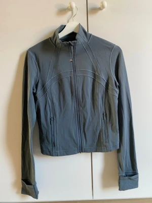 Grå blå träningsjacka från Lululemon - Snygg grå blå lululemon träningsjacka. Färgen är svår att få på bild. Kommer från ett djur och rökfritt hem. Använd endast tre gånger och tvättad mellan gångerna. Inte helt säker på storleken men skulle gissa på storlek 8. 