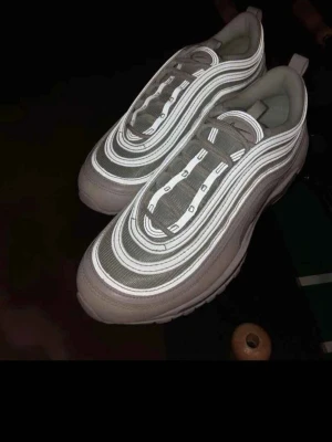 Nike Air Max 97 sneakers vita/grå - Nike Air Max 97 sneakers med ikoniska vågformade linjer och reflekterande detaljer. Finns i både helvitt och grått med vita inslag. Ovandel i mesh och syntet, synlig Air Max-sula för extra komfort. Perfekta för dig som gillar streetwear och sportig stil.