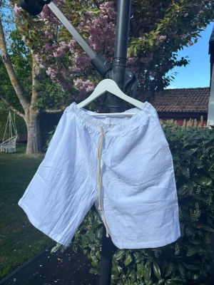Vita linneshorts med snörning - Säljer ett par vita shorts i linne med elastisk midja och snörning framtill. De har en loose passform och är perfekta för varma sommardagar. Stilrena och enkla att matcha med olika toppar. Helt nya, för stora för mig.