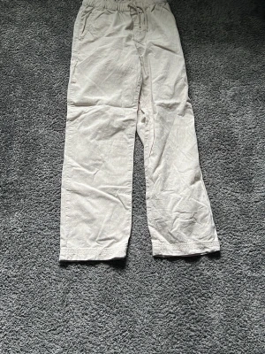 Beiga linnebyxor med resårmidja - Snygga beiga linnebyxor med avslappnad passform och resår i midjan samt dragsko. Byxorna har raka ben och sidfickor, perfekta för en chill och stilren look. Tillverkade i ett lätt och luftigt linnematerial.