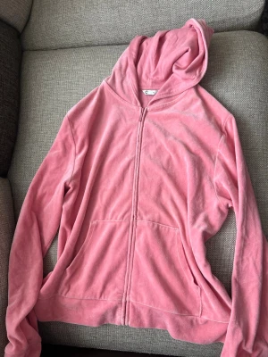 Rosa velourhoodie med dragkedja - Mjuk rosa hoodie i velour med dragkedja framtill och två fickor. Perfekt för en chill och avslappnad stil. Har huva och långa ärmar. Enkel och snygg design som passar till många outfits.