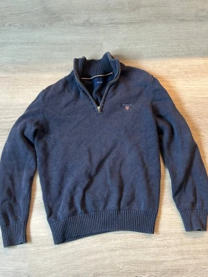Gant half zip - Mörkblå stickad tröja från Gant med halv dragkedja och ståkrage. Tröjan har ribbade muddar vid ärmslut och nederkant samt en liten broderad logga på bröstet. Perfekt för lager på lager och snygg till jeans.