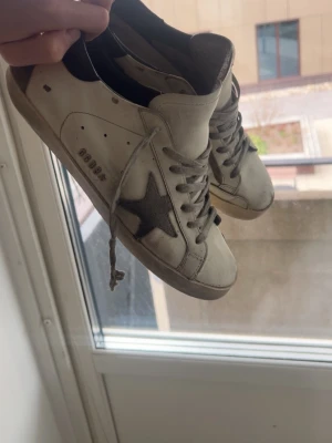 Golden goose - Snygga vita sneakers från Golden Goose med grå mockadetaljer och ikonisk stjärna på sidan. Skorna har grå snörning, svart hälparti och klassisk låg siluett. Perfekta för en trendig streetstyle-look.